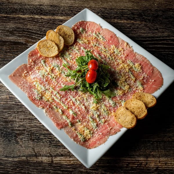 Caffe Gourmet's beef carpaccio, topped with cheese, pesto, arugula, cherry tomatoes, and toasted bread.