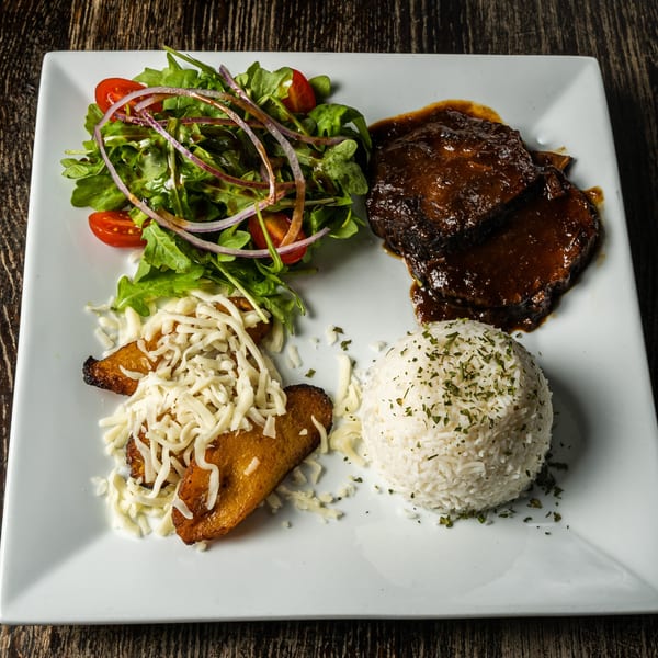 Venezuelan dish with braised meat, white rice, plantains with cheese, and a fresh salad.